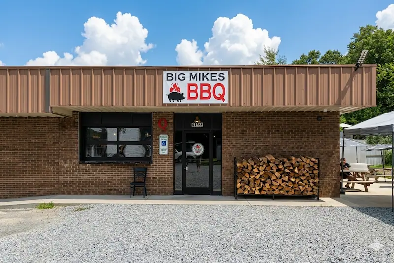 Exterior storefront view of Big Mike's BBQ in Mills River, NC, featuring a clean brick facade, a red and black Big Mikes sign with a pig logo, and a visible street address of 4176.